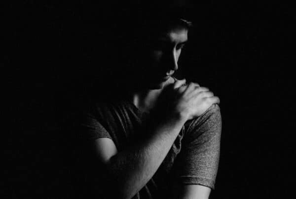 Man in a black background holding his shoulder in pain.